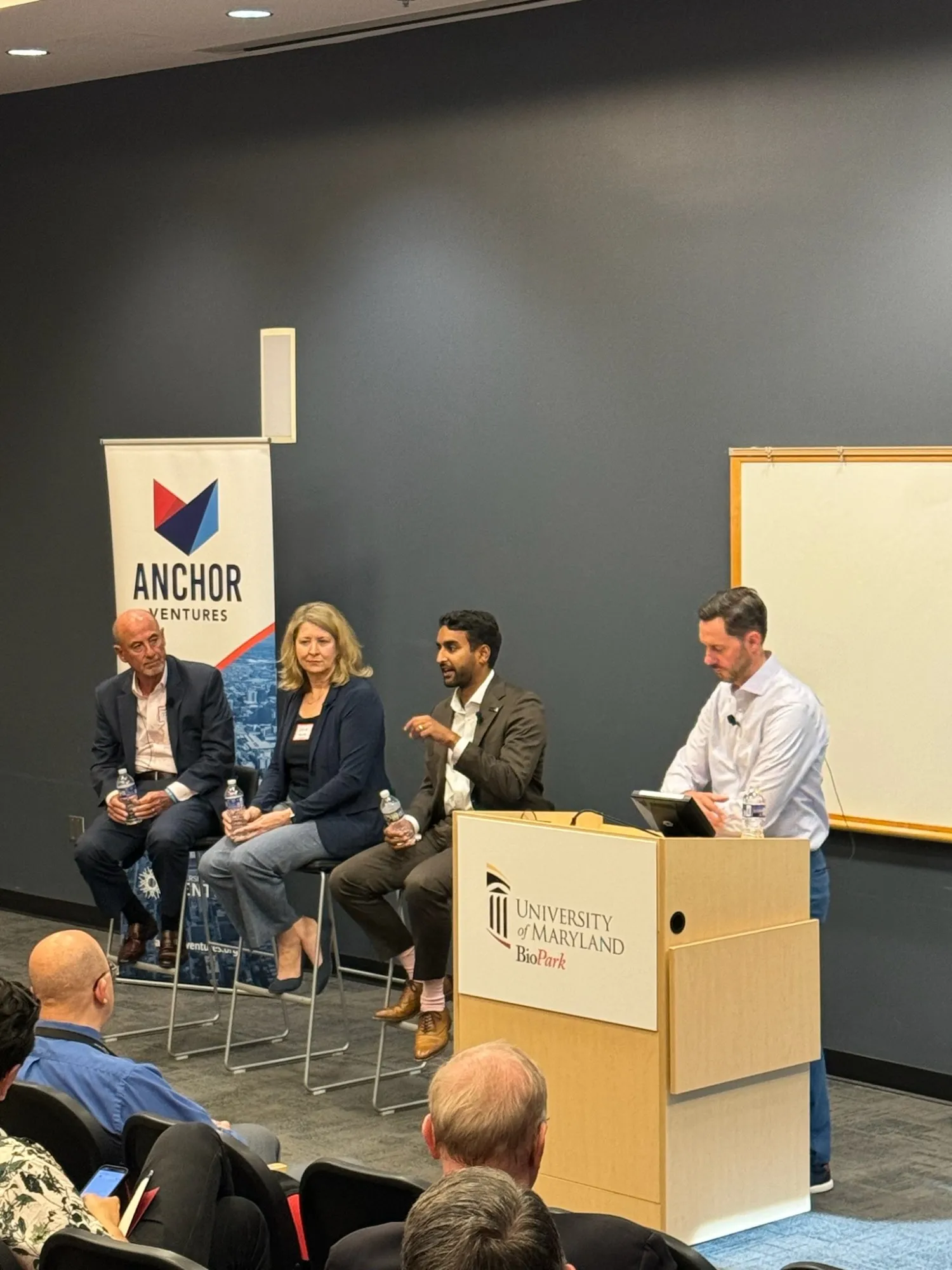 Four panelists on stools beside a moderator at a wooden podium at the University of Maryland BioPark