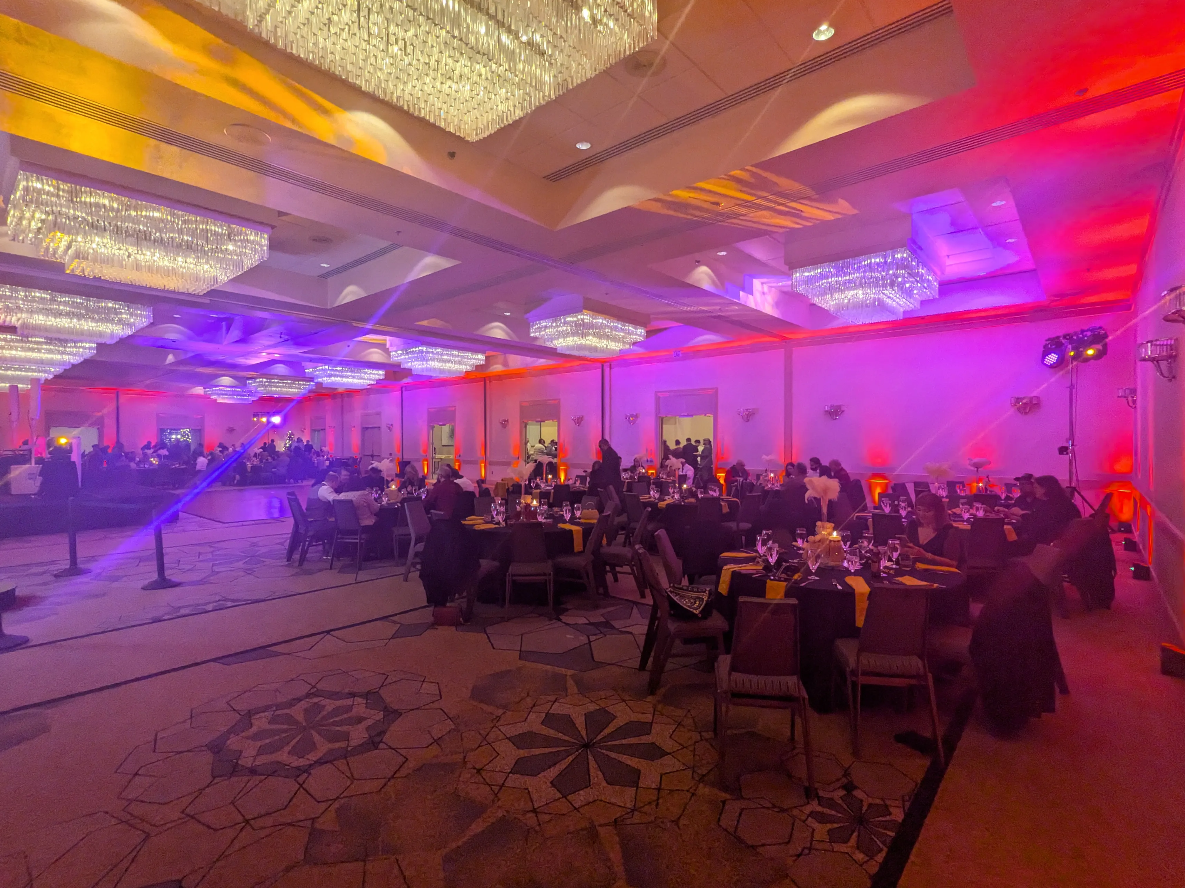 Hotel ballroom transformed with amber and violet uplighting for a corporate holiday party, a moving-head fixture rigged house-right