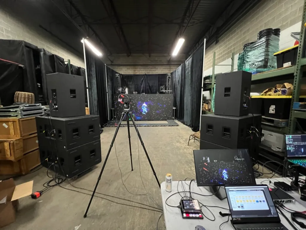 LED video wall panels lit with test content between line-array speaker stacks and a camera on tripod during pre-production in the shop