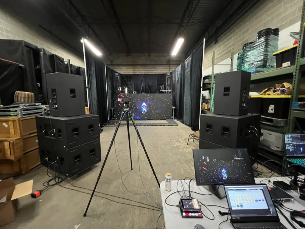LED video wall panels lit with test content between line-array speaker stacks and a camera on tripod during pre-production in the shop