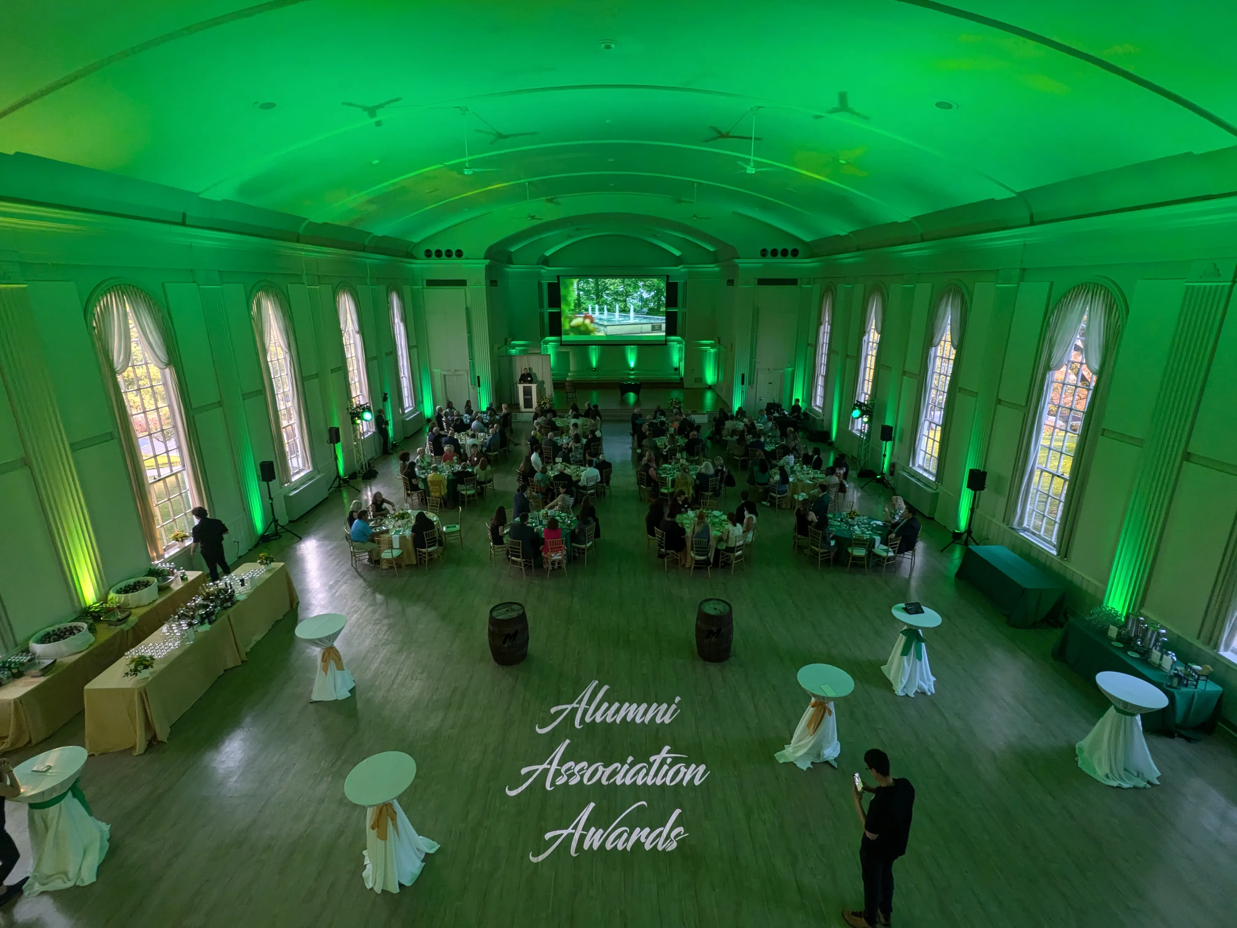 Awards dinner in a historic college hall with PA speakers on stands flanking the room and green uplighting on the walls